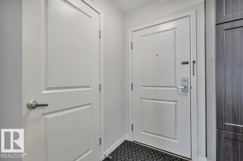 Entryway featuring a panel door with brushed nickel hardware, a secure entry door with a deadbolt and chain lock, and dark wood-finish cabinetry - 219 1820 Rutherford Road, Edmonton, AB 