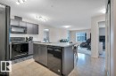 Kitchen with dark-finish cabinetry, black appliances, white subway tile backsplash, and a central island with integrated sink and dishwasher - 219 1820 Rutherford Road, Edmonton, AB 