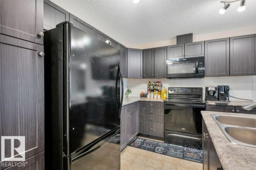 Kitchen featuring dark wood-finish cabinetry, black appliances, light-toned countertops, and a subway tile backsplash - 219 1820 Rutherford Road, Edmonton, AB 