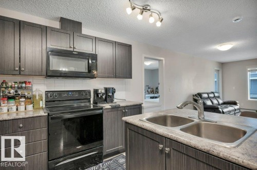 Kitchen featuring dark wood-finish cabinetry, a double basin sink, and a black appliance suite including an oven range and microwave - 219 1820 Rutherford Road, Edmonton, AB 