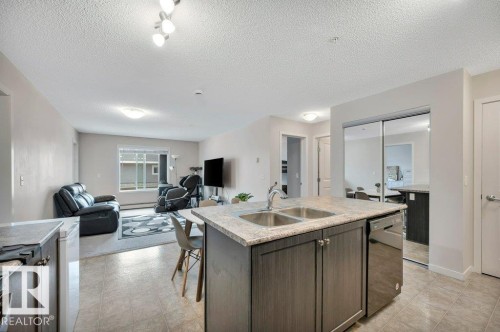 Kitchen island featuring a dual basin stainless steel sink, built-in dishwasher, and stone-finish countertop - 219 1820 Rutherford Road, Edmonton, AB 