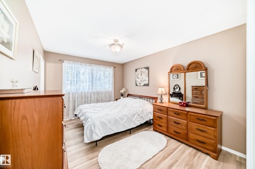 Bedroom featuring wood-finish flooring, a ceiling-mounted light fixture, and a window with sheer curtains - 9813 152 Street, Edmonton, AB 