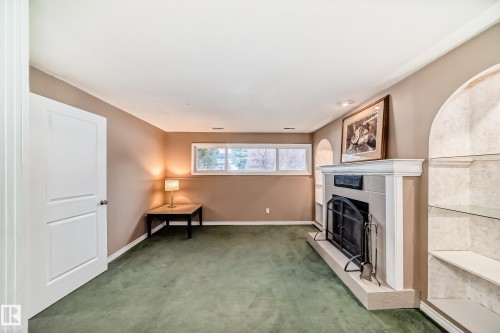Spacious room featuring a fireplace with a light-toned surround, an integrated fire screen, and a hearth - 9813 152 Street, Edmonton, AB 