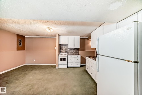 Kitchenette featuring white cabinetry, white electric range, white refrigerator, dark countertops, and a patterned backsplash - 9813 152 Street, Edmonton, AB 