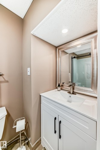 Modern bathroom featuring a white vanity with black hardware, a rectangular undermount sink, a chrome faucet, and a large framed mirror - 9813 152 Street, Edmonton, AB 
