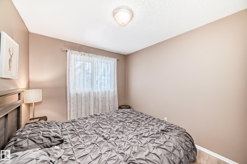 Bedroom featuring light-colored walls, a window with sheer curtains, wood-finish flooring, and a ceiling-mounted light fixture - 9813 152 Street, Edmonton, AB 