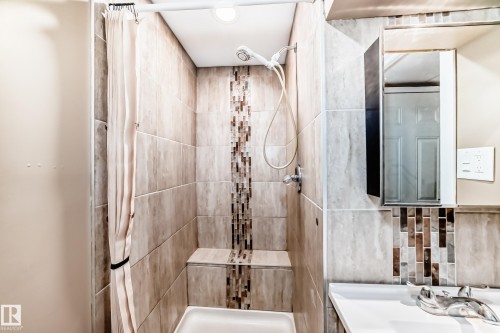 Tiled shower enclosure featuring a mosaic accent strip, built-in bench, and a handheld showerhead - 9813 152 Street, Edmonton, AB 