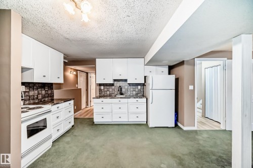 Kitchen featuring white cabinetry, dark stone-finish countertops, tiled backsplash, white appliances, and a drop ceiling with a three-light fixture - 9813 152 Street, Edmonton, AB 