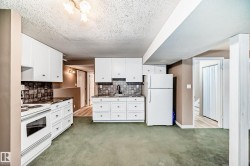 Kitchen featuring white cabinetry, dark stone-finish countertops, tiled backsplash, white appliances, and a drop ceiling with a three-light fixture - 