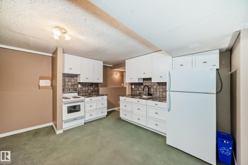 Kitchenette featuring white cabinetry with dark hardware, a white electric range, a white refrigerator, and a dark sink with a black faucet - 9813 152 Street, Edmonton, AB 