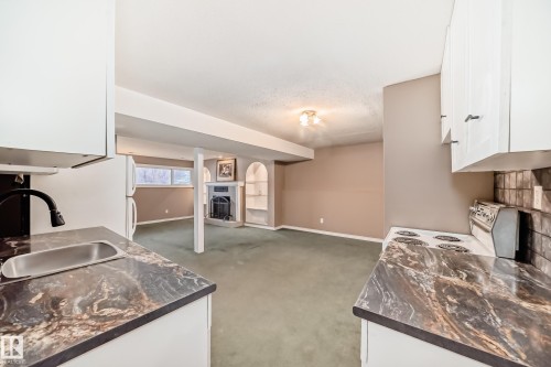 Kitchenette featuring white cabinetry, dark veined countertops, and a stainless steel sink with a black gooseneck faucet - 9813 152 Street, Edmonton, AB 