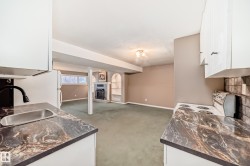 Kitchenette featuring white cabinetry, dark veined countertops, and a stainless steel sink with a black gooseneck faucet - 