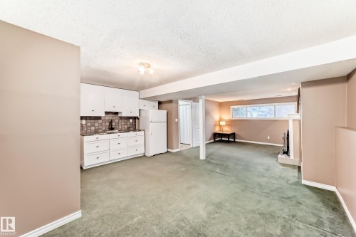 Spacious lower level featuring a functional kitchenette with white cabinetry, a dark tile backsplash, and a white refrigerator - 9813 152 Street, Edmonton, AB 