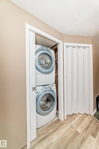 Dedicated laundry closet featuring a stacked washer and dryer, wood-finish flooring, and a nearby storage closet with bi-fold doors - 9813 152 Street, Edmonton, AB 