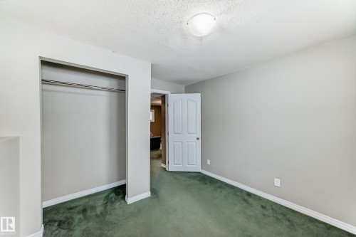 Room featuring green carpeting, light gray walls, white baseboards, and a built-in closet with a metal hanging rod - 9813 152 Street, Edmonton, AB 