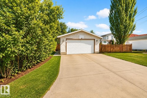 Detached garage with a paneled door, complemented by a concrete driveway, manicured lawn, and mature perimeter trees and shrubs - 9813 152 Street, Edmonton, AB 