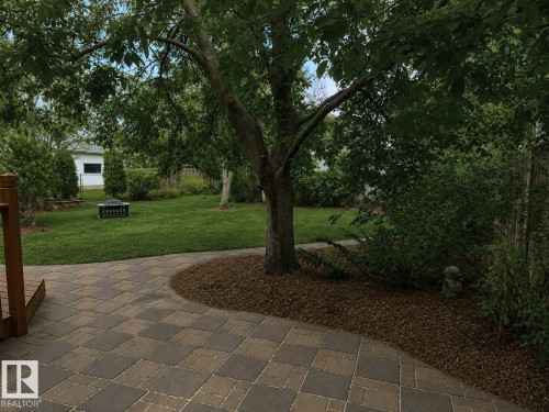Spacious backyard featuring a paver patio, manicured lawn, established trees, and mature landscaping - 9813 152 Street, Edmonton, AB 