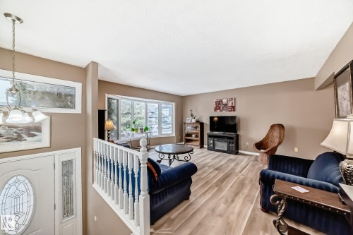 Open-concept living area featuring wood-finish flooring, a large bay window, and a white baluster railing - 9813 152 Street, Edmonton, AB 