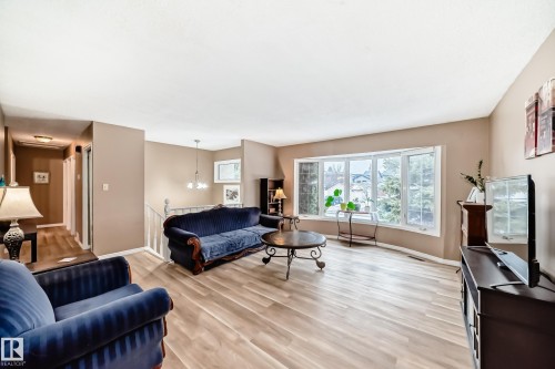 Spacious living area featuring light wood-finish flooring, a large bay window with multiple panes, neutral wall tones, a built-in railing system, and a ceiling-mounted light fixture - 9813 152 Street, Edmonton, AB 