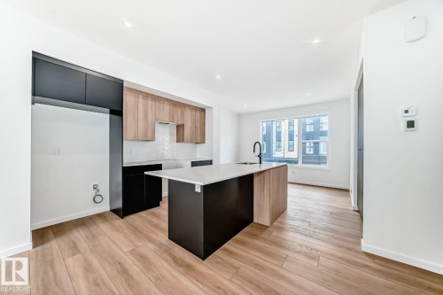 Contemporary kitchen featuring a central island with a sink and matte black faucet, light wood-finish flooring, recessed lighting, and a window providing natural light - #66 5 Rondeau Dr, St. Albert, AB - Indoor Photo Showing Kitchen