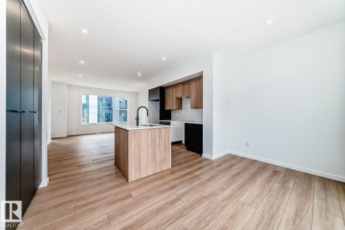 Modern kitchen island with a white countertop and integrated sink, complemented by wood-finish base cabinetry and matte black hardware - #66 5 Rondeau Dr, St. Albert, AB - Indoor Photo Showing Kitchen