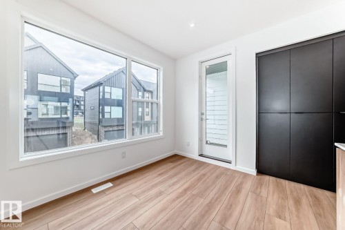 Bright interior space featuring a large picture window, wood-finish flooring, a white trim package, a glass-paneled exterior door, and built-in dark panel cabinetry - #66 5 Rondeau Dr, St. Albert, AB - Indoor Photo Showing Other Room