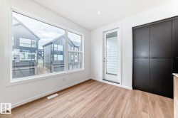 Bright interior space featuring a large picture window, wood-finish flooring, a white trim package, a glass-paneled exterior door, and built-in dark panel cabinetry - 