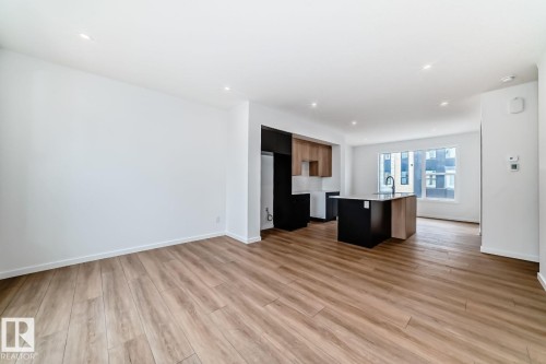 Spacious open-concept living area featuring wood-finish flooring, recessed lighting, and a kitchen with a dark-finish island, light-toned countertops, and a window providing natural illumination - #66 5 Rondeau Dr, St. Albert, AB - Indoor