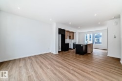 Spacious open-concept living area featuring wood-finish flooring, recessed lighting, and a kitchen with a dark-finish island, light-toned countertops, and a window providing natural illumination - 