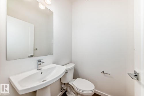 Powder room featuring a pedestal sink with a modern chrome faucet, a rectangular mirror, and an overhead light fixture - #66 5 Rondeau Dr, St. Albert, AB - Indoor Photo Showing Bathroom