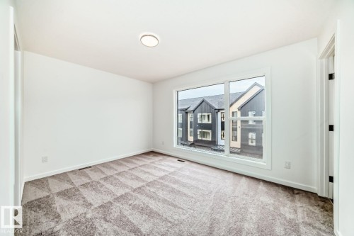 Bright room featuring a large window, neutral white walls, and geometric pattern carpeting - #66 5 Rondeau Dr, St. Albert, AB - Indoor Photo Showing Other Room