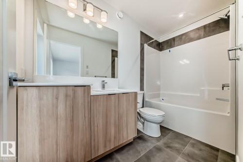 Bathroom featuring a wood-finish double vanity with white countertops, a large rectangular mirror, and a tub-shower combination with dark tile surround - #66 5 Rondeau Dr, St. Albert, AB - Indoor Photo Showing Bathroom