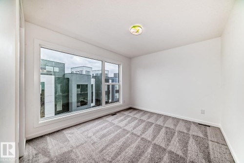 Spacious room featuring a large picture window, patterned carpet flooring, white walls, and a ceiling-mounted light fixture - #66 5 Rondeau Dr, St. Albert, AB - Indoor Photo Showing Other Room