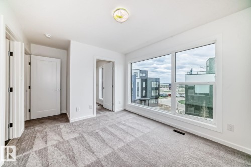 Spacious room featuring a large picture window, patterned carpeting, white walls, and contemporary doors - #66 5 Rondeau Dr, St. Albert, AB - Indoor Photo Showing Other Room