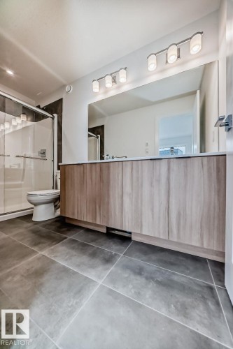 Bathroom featuring a wood-finish double vanity with a light-toned countertop, a large wall-mounted mirror, and a four-bulb vanity light fixture - #66 5 Rondeau Dr, St. Albert, AB - Indoor