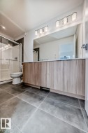 Bathroom featuring a wood-finish double vanity with a light-toned countertop, a large wall-mounted mirror, and a four-bulb vanity light fixture - 