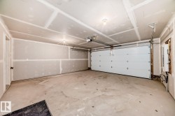Spacious two-car garage featuring a sectional garage door, concrete flooring, and unfinished drywall walls and ceiling - 