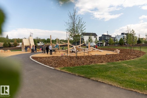 Contemporary natural playground featuring wooden play structures, wood chip surfacing, and a dedicated paved pathway - #66 5 Rondeau Dr, St. Albert, AB - Outdoor