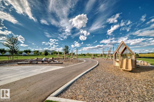 Recreational park area featuring a play structure with a double slide, a swingset, natural wood log climbing features, and a paved pathway - #66 5 Rondeau Dr, St. Albert, AB - Outdoor With View