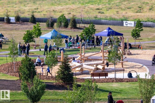 Outdoor park space featuring a natural-style playground with log structures, wood chip surfacing, paved walkways, and mature trees - #66 5 Rondeau Dr, St. Albert, AB - Outdoor With View