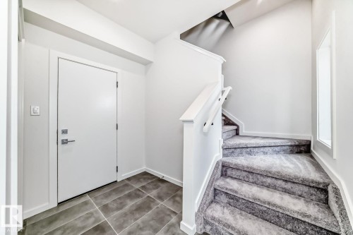 Entryway featuring a white door with brushed nickel hardware, grey tile flooring, and a carpeted staircase with white railings - #66 5 Rondeau Dr, St. Albert, AB - Indoor Photo Showing Other Room