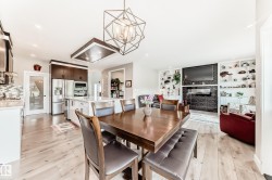 Open-concept living space with wood-finish flooring, a contemporary geometric chandelier, and built-in shelving surrounding a linear fireplace - 