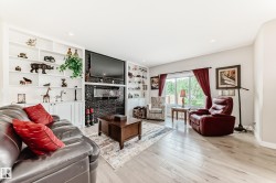 Living area featuring light wood-finish flooring, recessed lighting, and a prominent fireplace with a dark, textured surround - 