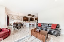 Open-concept living space featuring wood-finish flooring, a dining area with a geometric chandelier, and an island kitchen with dark cabinetry and stainless steel appliances - 