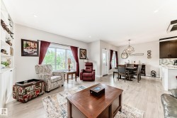 Open-concept living area featuring light wood-finish flooring, a built-in shelving unit, recessed lighting, and a dining area with a modern chandelier - 