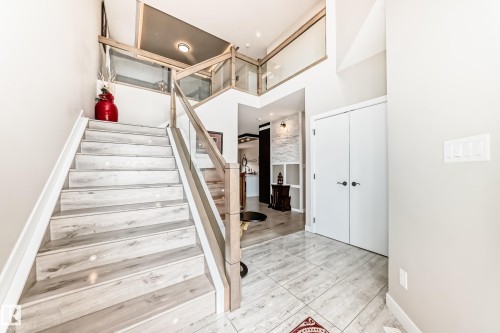 Two-story foyer featuring wood-finish flooring on the staircase, glass panel railings with light wood handrails, and a tiled entry floor - 3895 Robins Crescent, Edmonton, AB 