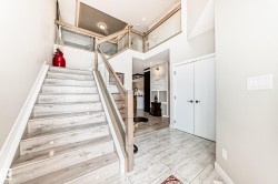Two-story foyer featuring wood-finish flooring on the staircase, glass panel railings with light wood handrails, and a tiled entry floor - 