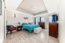 Spacious room featuring light wood-finish flooring, a tray ceiling with a central flush-mount light fixture, and two windows - 