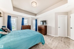 Recessed tray ceiling, multiple windows with white trim, light wood-finish flooring, and white interior doors with black hardware - 