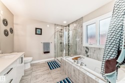 Bathroom featuring a built-in tub, separate glass-enclosed shower, dual-sink vanity with white cabinetry, and wood-finish tile flooring - 